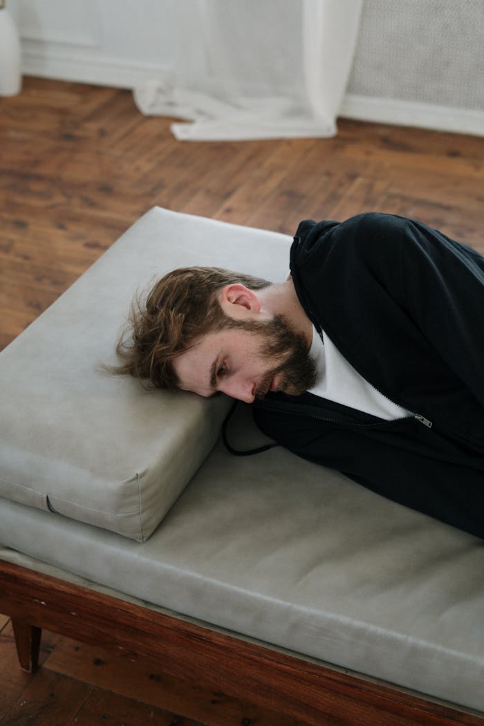 A man lies on a couch indoors, appearing deep in thought or contemplative mood.