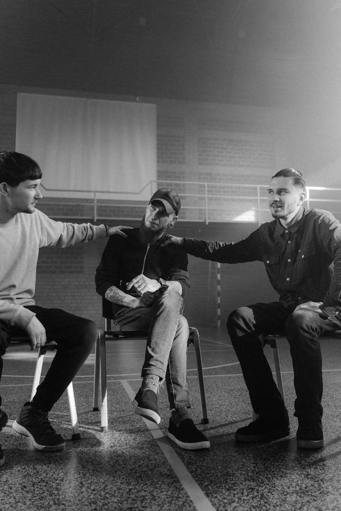Three men participating in a supportive group therapy session indoors, captured in grayscale.